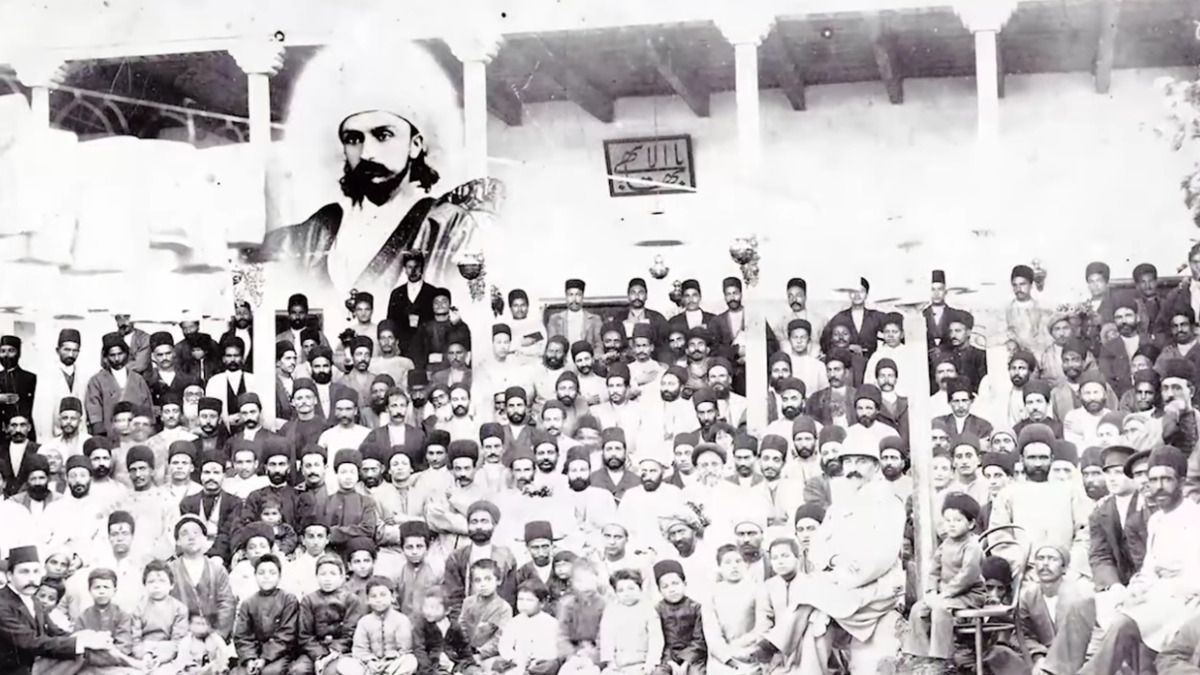 لقطة تاريخية من الفيلم الوثائقي البهائي مائتا عام من التاريخ الخفي تظهر تجمعاً قديماً مع صورة رمزية في الخلفية.