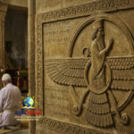 نقش حجري لرمز الفراوفهر الزرادشتي على جدار معبد مع شخص يصلي وشعلة النار المقدسة في الخلفية.