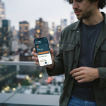 A young US freelancer uses the Cashably financial tools app on his phone with a city skyline in the background.