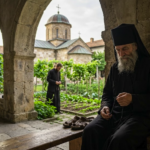 An elderly Orthodox monk holding prayer beads sitting on a bench, illustrating what happens inside closed monasteries.
